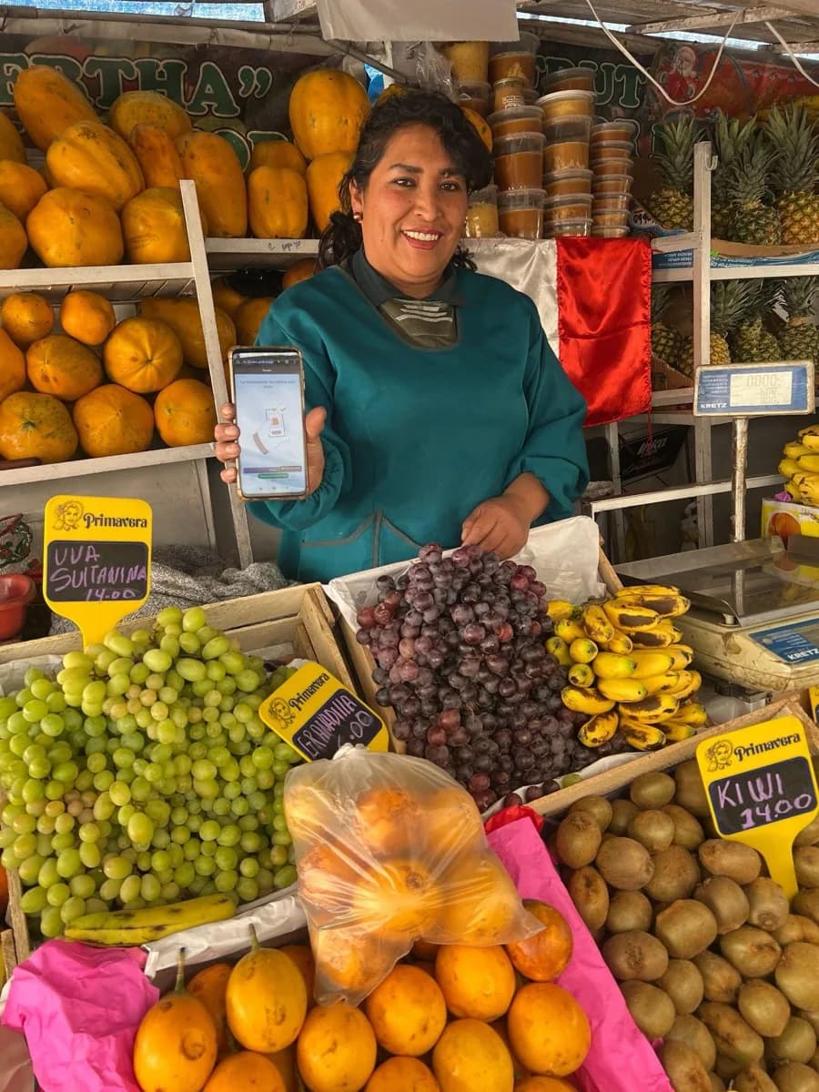 Uma vendedora de frutas em um mercado de Cusco mostrando o aplicativo da carteira em seu celular