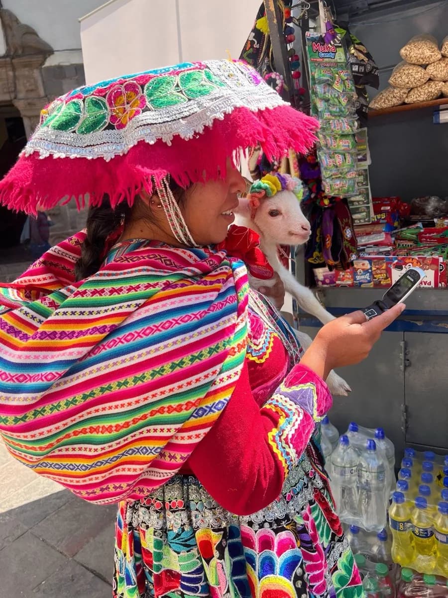 Uma mulher quéchua em trajes tradicionais usando um celular básico em Cusco
